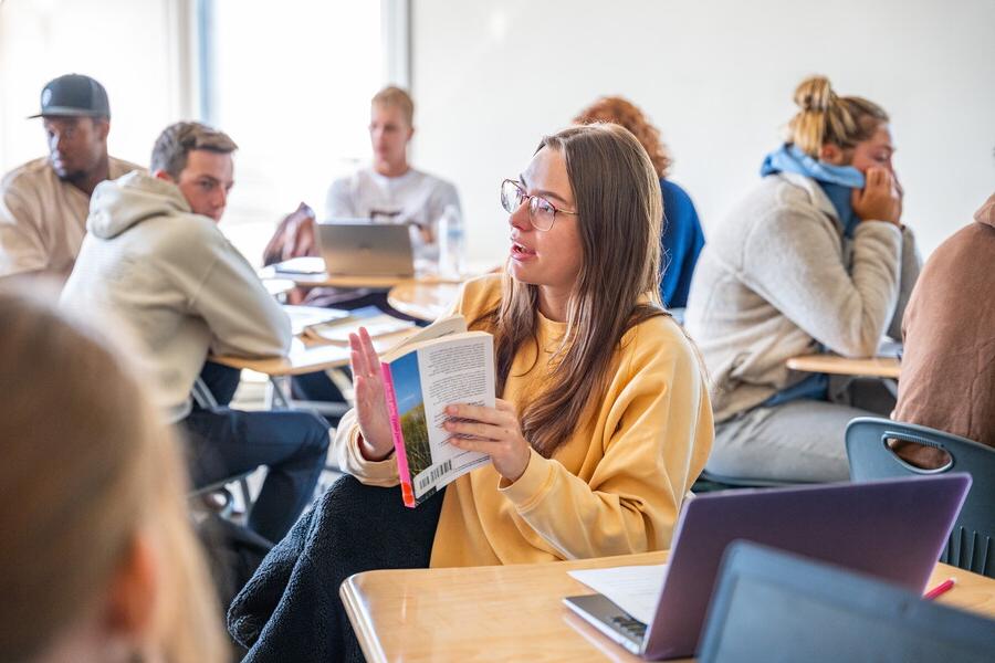 A student in a classroom talking to classmates.